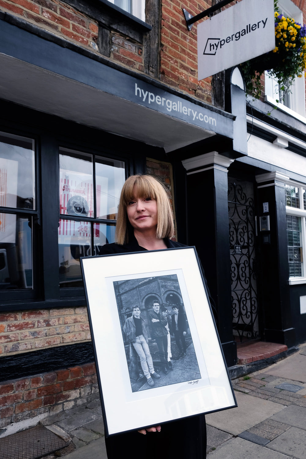 Emily from Hypergallery outside the print room with a framed copy of Stephen Wright's photograph of The Smiths for The Queen Is Dead album cover in front of Salford Lads Club