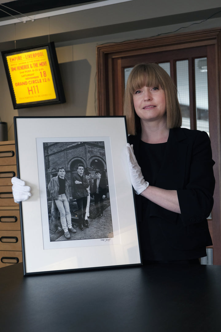 Emily from Hypergallery in the print room with a framed copy of Stephen Wright's photograph of The Smiths for The Queen Is Dead album cover in front of Salford Lads Club